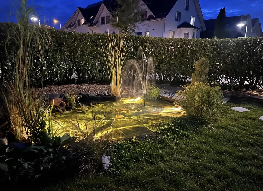 Beleuchteter Gartenteich mit Wasserspiel am Abend