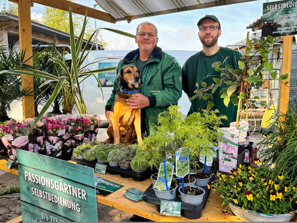 Das Team von Passionsgärtner mit Hund zwischen Pflanzen am Verkaufsstand